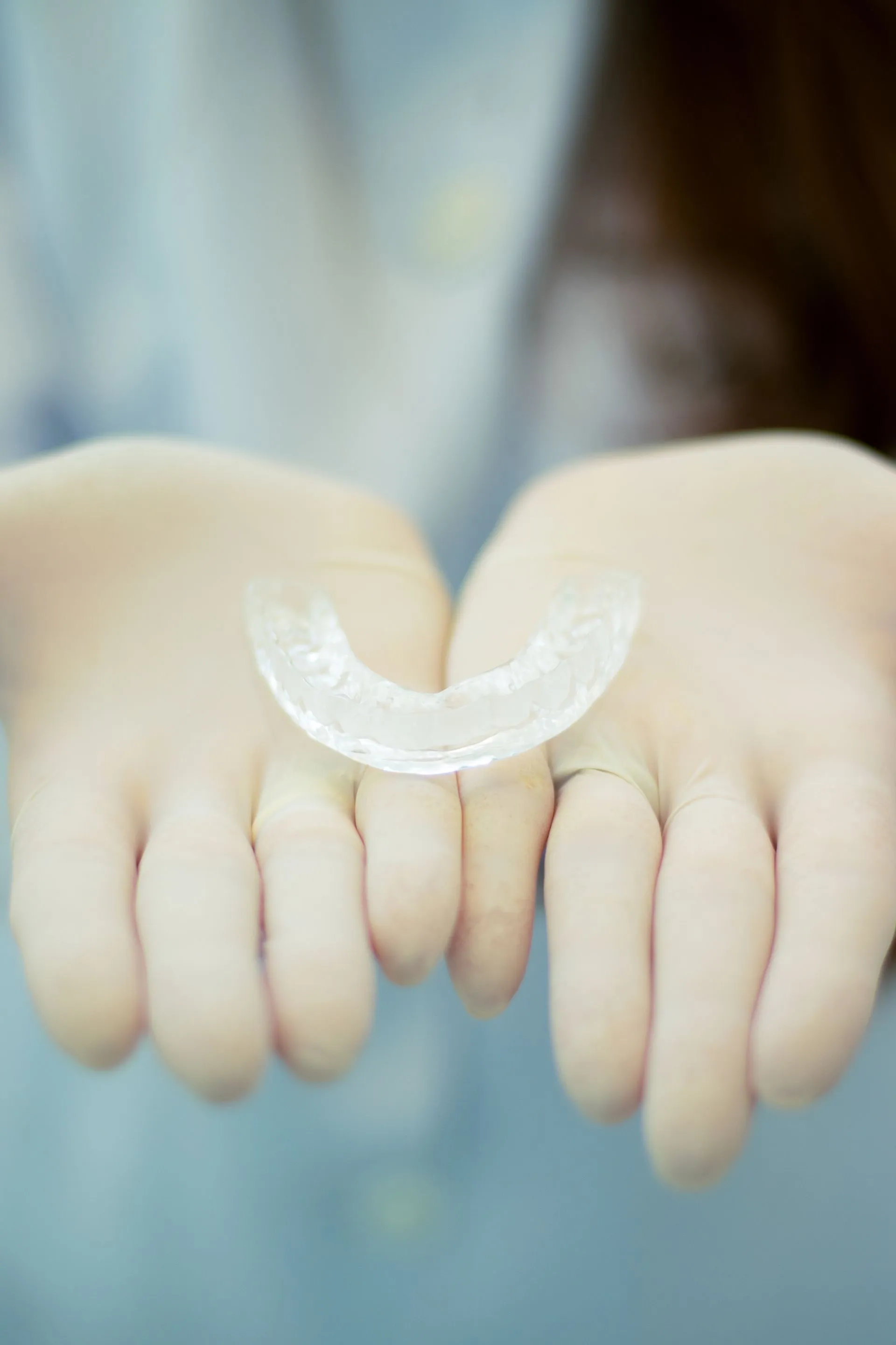 Manos con guantes sosteniendo una férula de descarga dental transparente